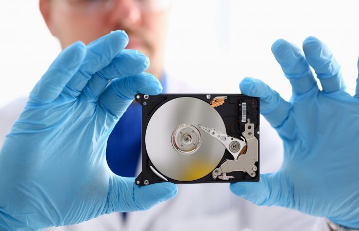 A male repairman wearing blue gloves is holding a hard drive from computer or laptop in hands. Performs fault diagnostics and performs urgent repairs recovery of lost data during deletion HDD closeup